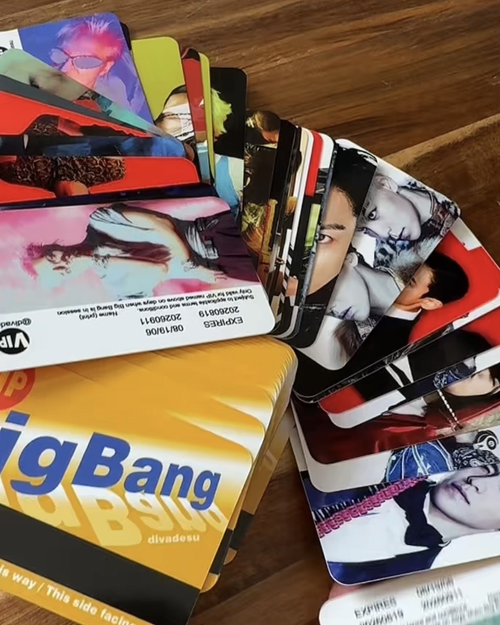 A stack of colorful printed cards or photo strips fanned out on top of a yellow card labeled 'Big Bang' on a wooden surface.
